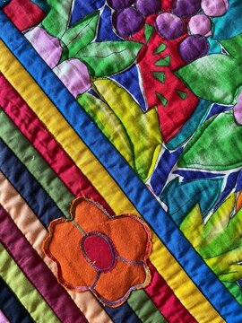 Close-up of a vibrant colorful quilt featuring rainbow striped borders, appliqu&eacute; flowers, leaves, and fruit motifs in bright fabric patches 