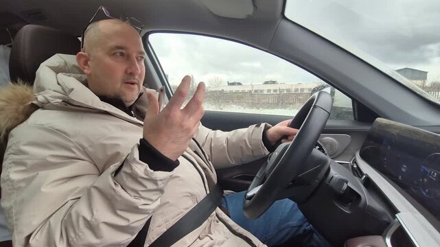 Middle aged man talks while driving his car in wintery urban surroundings. Steady interior camera shot.
