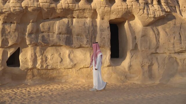 Cinematic close-up of Saudi man in red shemagh walking and examining intricate stone carving details of ancient tombs in Madain Saleh AlUla