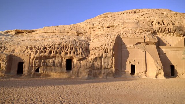 Wide panning shot of ancient Nabataean rock-cut tombs carved into sandstone mountain in Hegra, AlUla