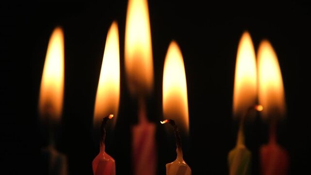 Birthday candles burning brightly against a black background before extinguishing one by one with glowing wicks and fading smoke in darkness. High quality FullHD footage