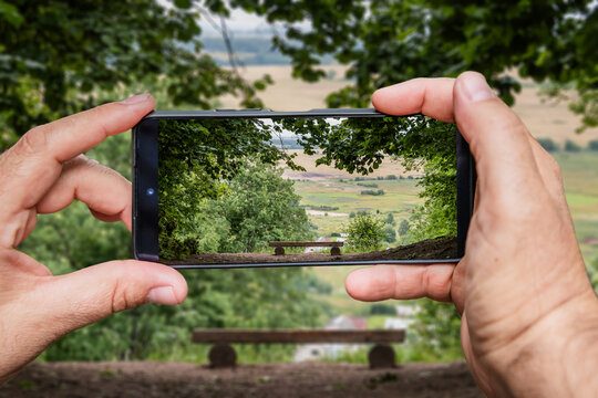 Man holding smartphone taking photo of beautiful summer landscape with bench