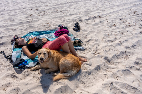 Woman Relaxing With Golden Dog On Sandy Beach During Summer Pet Vacation And Leisure
