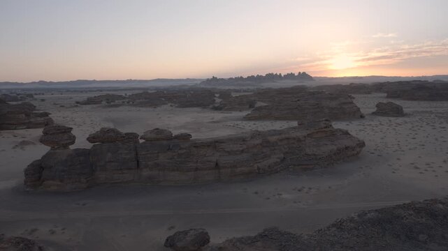 Cinematic wide aerial drone shot of unique flat top mushroom rock formations over desert sand at dawn twilight in Madain Saleh AlUla
