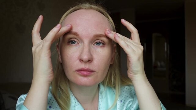 Adult woman touching facial wrinkles on forehead and between eyebrows. She does anti aging massage and considers botox injection.
