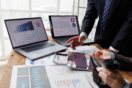 Business people collaborating on financial strategy, analyzing market data and performance reports displayed on laptops and digital tablets in a modern office meeting