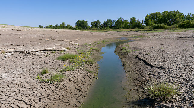 Severe drought with cracked dry earth and a small dwindling stream in a barren landscape, symbolizing climate change and water scarcity