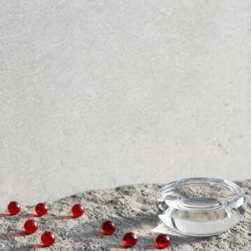 Clear glass bowl with red gelatin spheres on a textured concrete surface, minimalist product display for pharmaceutical or skincare branding