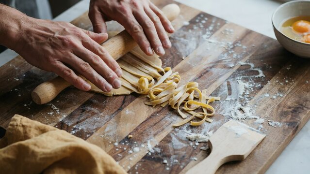 Hands using a rolling pin to flatten fresh pasta dough on board
