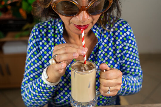 Woman refreshing with cold coffee while wearing colorful shirt and stylish sunglasses