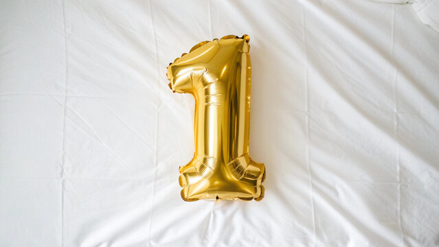 Golden number 1 balloon isolated on soft pastel background, glossy foil texture, festive celebration concept, minimal composition with elegant lighting and copy space.