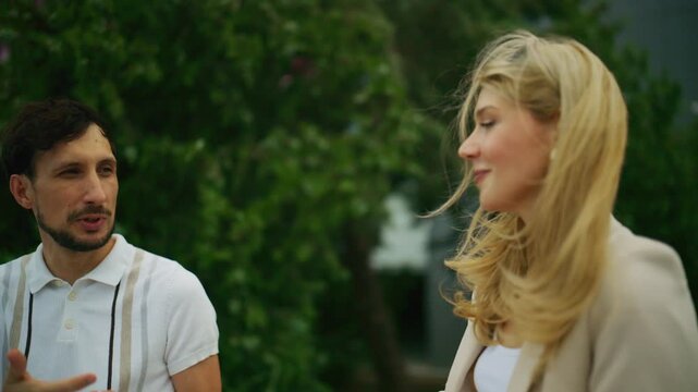 Two business people engage in a discussion outdoors, appearing focused on their work. They are two young professionals having a conversation.