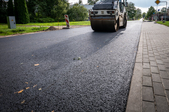 Heavy Road Roller Compacts Fresh Asphalt Beside a Paved Sidewalk