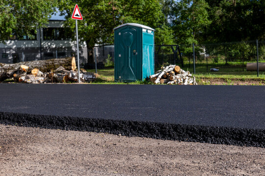 Fresh Asphalt Path Beside a Portable Toilet and Cut Logs