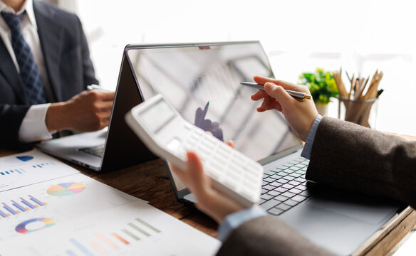 Business professionals analyzing financial data on a laptop and printed charts, using a calculator and pen for strategic planning and accounting tasks in a modern office