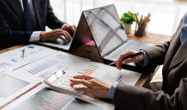 Business professionals analyzing financial data and market reports on documents and laptop, calculating numbers, planning company strategy for corporate success and growth