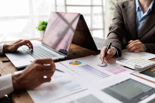 Business professionals collaborating at a desk, reviewing charts and reports on a laptop and paper, discussing market trends, strategy and financial planning for growth and development