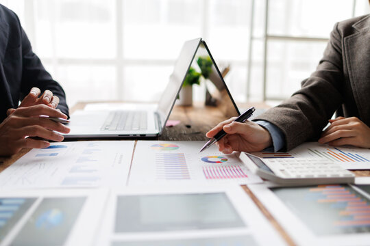 Business professionals meeting, discussing financial graphs and charts on paper documents, analyzing data for strategic planning and successful collaboration in an office environment