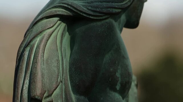 Bronze winged statue in closeup with weathered surface and soft outdoor background