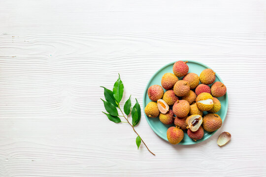 Fresh lychee fruit with green leaves on a plate, top view