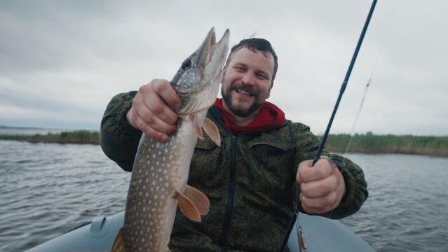 Fisherman sits in the boat on the lake and holds the trophy pike fish