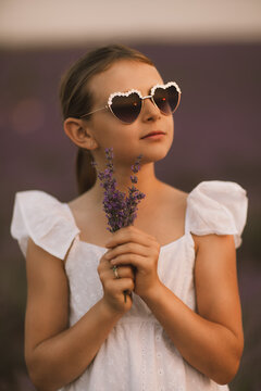 Heart shaped sunglasses worn by young girl holding lavender flowers in blooming purple field during sunny afternoon