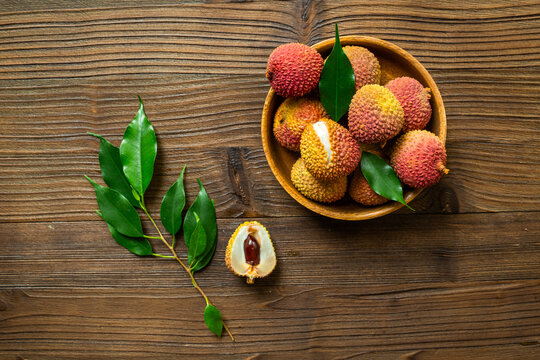 Fresh lychee fruit in bowl with green leaves, top view