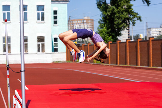 Teenage high jumper lands on back after clearing outdoor bar. Concept of youth athletics, Fosbury flop technique, safe landing, competition and sports training.