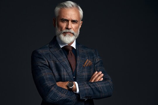 Sophisticated mature man with a grey beard wearing a textured blazer and tie against dark wall
