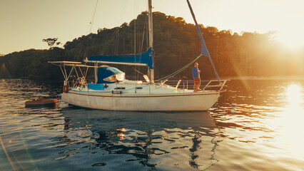 Man stands on the deck of the sailing boat and enjoys calm morning time in the secured lagoon on sunrise © Dudarev Mikhail