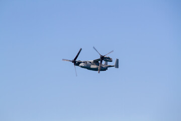 Fototapeta premium V-22 Osprey military tiltrotor aircraft flying against a clear blue sky, photographed in side profile with its distinctive twin rotors, engines, wings and rear fuselage clearly visible.