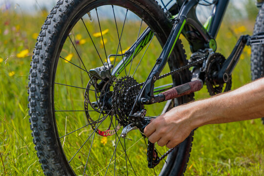 Close up of hand adjusting rear derailleur and chain cassette on mountain bike in green field, bicycle repair and maintenance concept