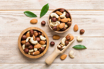 Fototapeta premium Assortment of nuts in wooden bowl on colored table. Cashew, hazelnuts, walnuts, almonds. Mix of nuts Top view with copy space