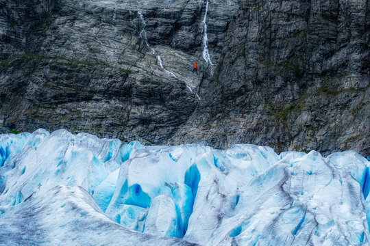 Dramatic landscape of rock climber climbing above glacier, Nigardsbreen, Norway