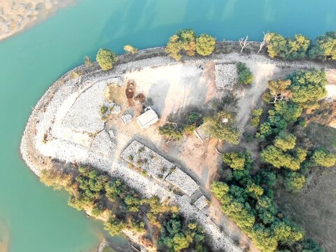 Aerial view of the Indus River bank featuring sandy terrain, sparse vegetation, and small structures along the water in Dera Ghazi Khan, Punjab, Pakistan.