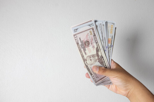 Hand holding a fan of US dollar bills against a white wall background with large copy space. Concept of wealth, salary payment, cash loan, financial success, and business investment.