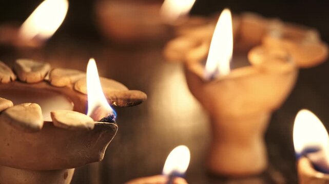Close up of a burning diya wick with soft flame and blurred lamps in background