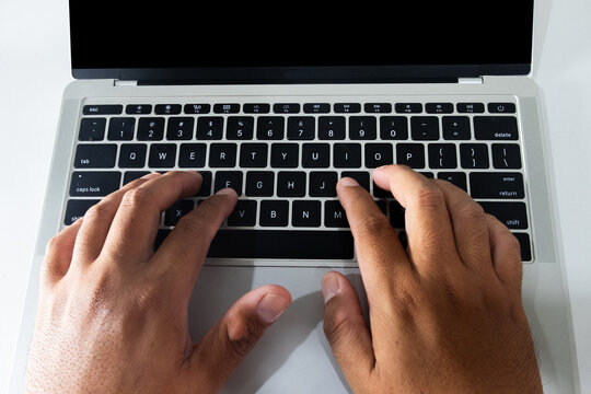 Top view close up of man hands typing on a silver laptop keyboard with a blank black screen. Concept of working from home, online business, coding, freelance copywriting, and internet surfing.