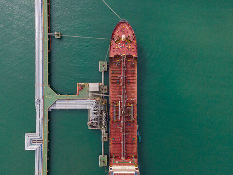 Aerial view of a large oil tanker docked at an industrial terminal with pipelines and storage infrastructure in the sea in Cilacap, Central Java, Indonesia.