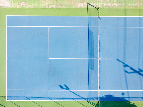 Aerial view of a blue tennis court with white lines and a net, surrounded by green court borders, captured from directly above in Klaten, Central Java, Indonesia.