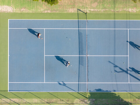 Aerial view of two tennis players on a blue court with white lines, net, and long shadows in Klaten, Central Java, Indonesia.