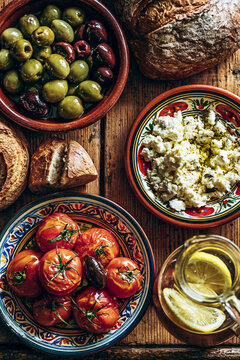 Flat lay shot of a rustic wooden table filled with Mediterranean dishes: green and Kalamata olives, tomatoes with olive oil, feta cheese and bread.