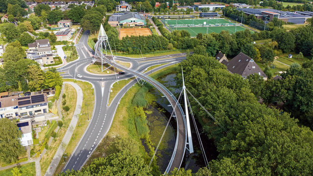 Aerial view of De Slinger Bicycle bridge spanning over a roundabout surrounded by lush trees and residential areas in Drachten, Friesland, Nederland.