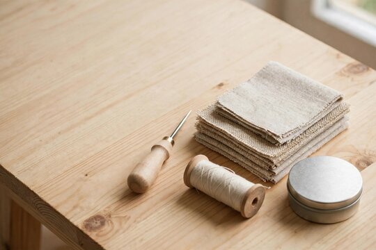 Wooden awl with thread spool and linen fabric swatches on wooden workbench for craft sewing project
