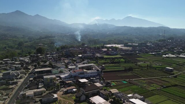 Aerial drone footage of rural village and green vegetable farmland with Mount Panderman background in Pujon, Malang