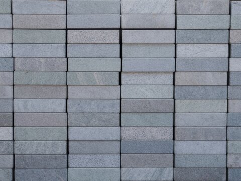 Top view of stacked uniform polished gray granite stone blocks arranged in neat vertical columns and horizontal rows, showcasing natural speckled mineral texture for construction materials.