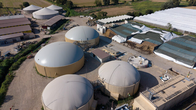 Aerial view of a biomethane production plant with large circular digester tanks and agricultural infrastructure in San Giuliano Milanese, Lombardy, Italy.