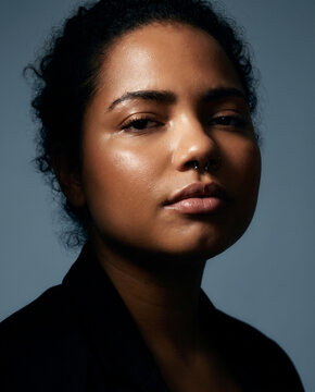 A stunning portrait of a woman with curly hair, a nose ring, and confident gaze, set against a subtle blue background