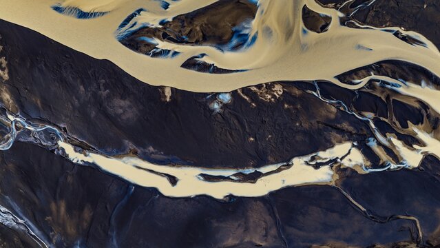 Aerial view of the braided Tungnaa river flowing through dark volcanic sand with glacial sediment patterns in Skaftarhreppur, Iceland.
