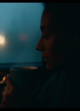 Close-up of a person's face, holding a cup of coffee. the person appears to be deep in thought, with their eyes closed and their head tilted slightly to the side.